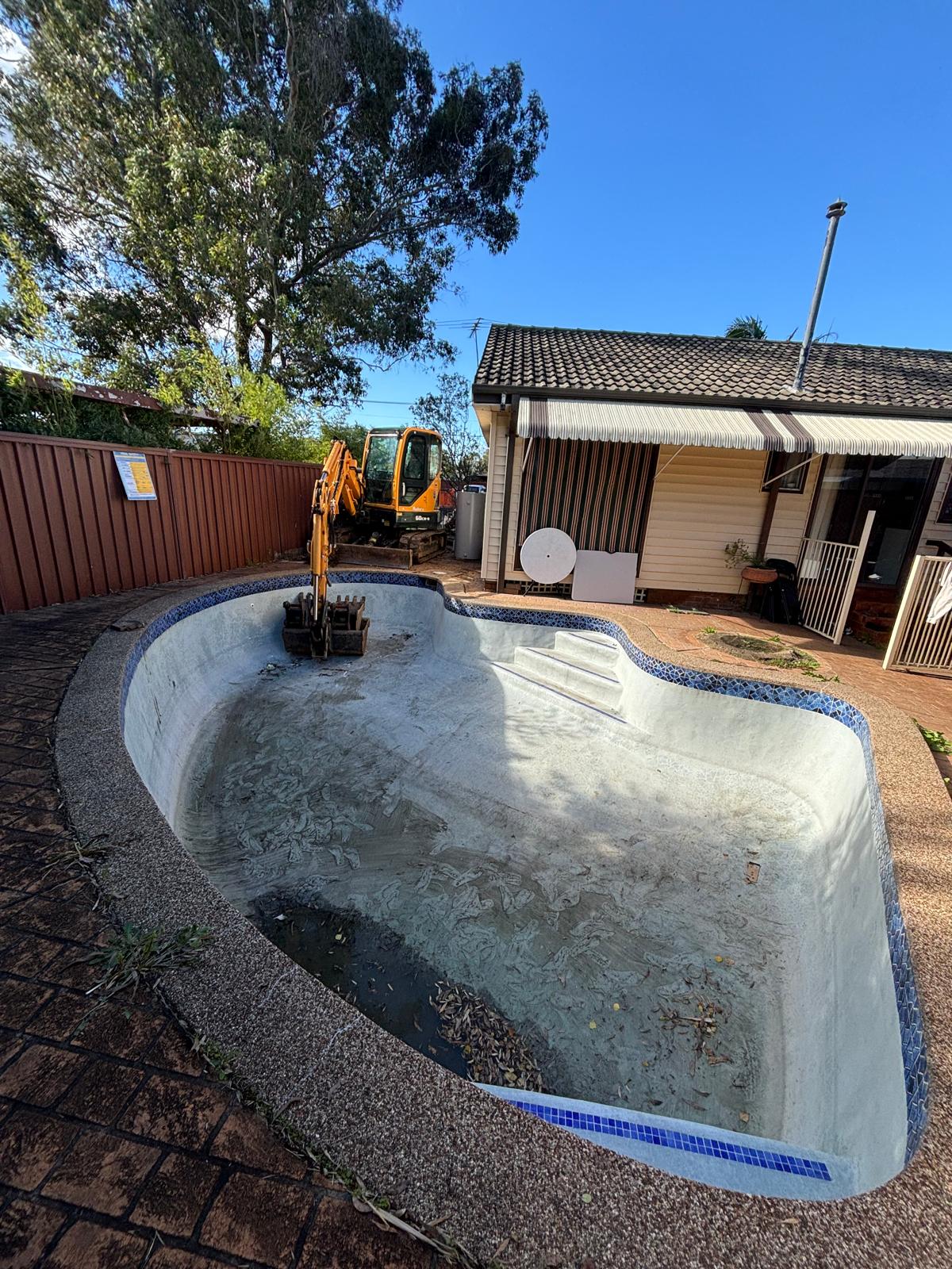 Excavator positioned inside a Sydney backyard pool ready to begin demolition