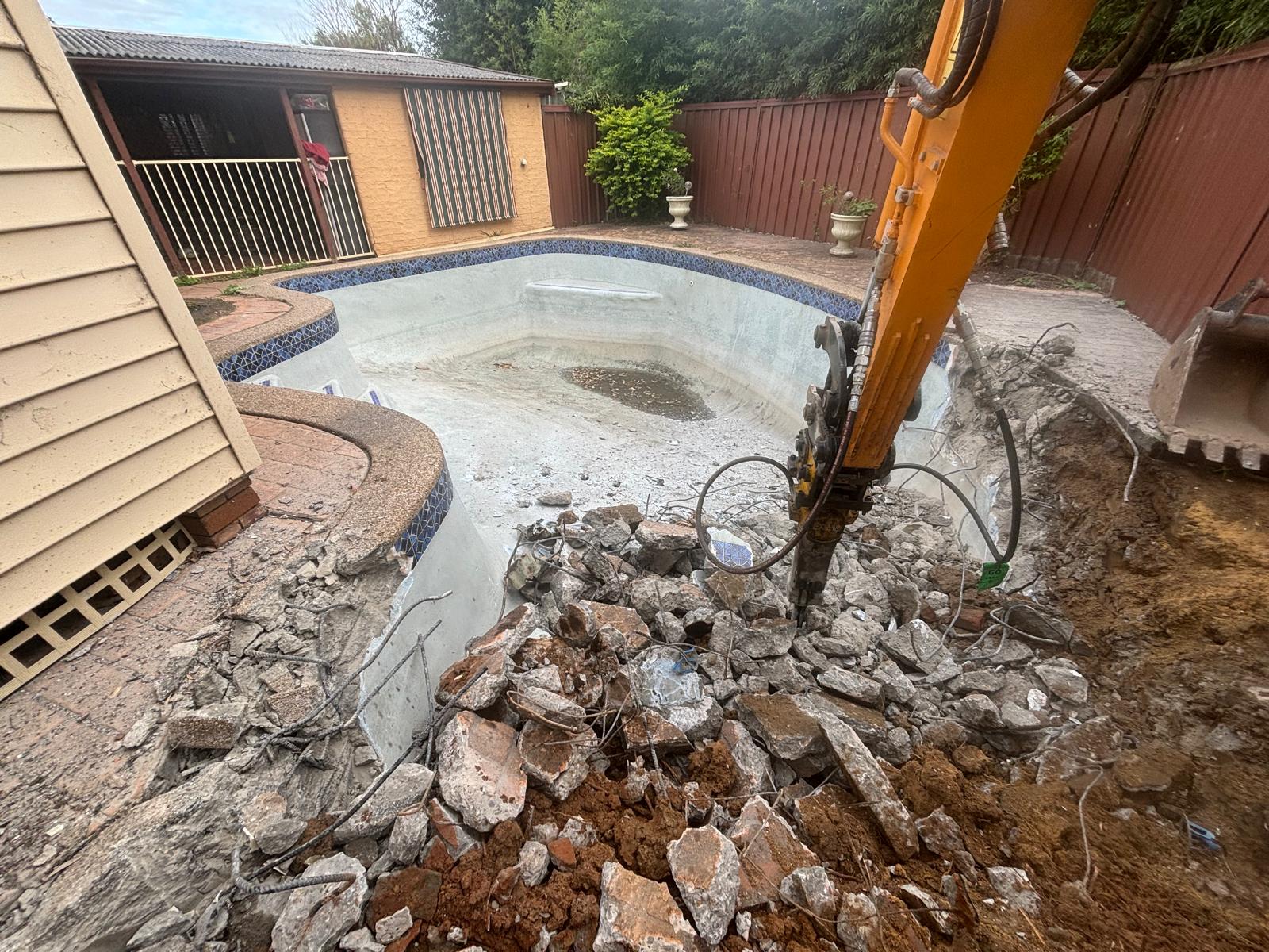 Hydraulic hammer breaking up a concrete pool shell during a Sydney pool removal
